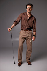 Fashionable man in golden chain and shirt holding golf club and dollars on grey 