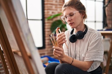 Young blonde woman artist looking paintbrushes at art studio