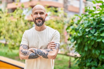 Young bald man standing with arms crossed gesture at park