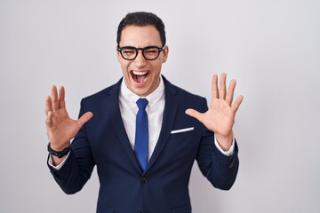 Young hispanic man wearing suit and tie celebrating mad and crazy for success with arms raised and closed eyes screaming excited. winner concept