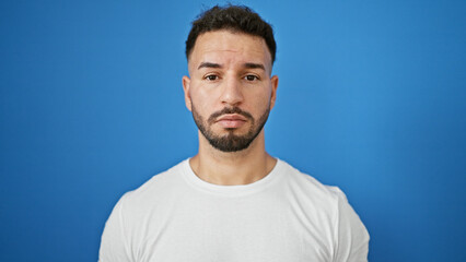 Young arab man standing with serious expression over isolated blue background