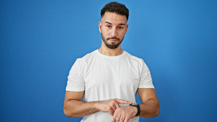 Young arab man pointing to watch with serious face over isolated blue background