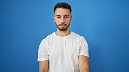 Young arab man standing with serious expression over isolated blue background