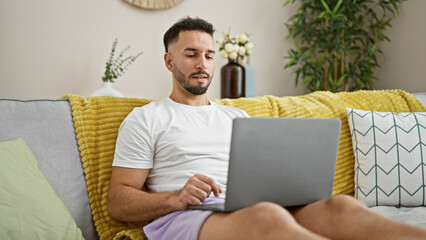 Young arab man using laptop sitting on sofa at home