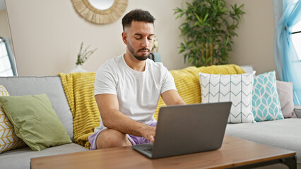 Young arab man using laptop sitting on sofa at home