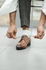 Closeup of the hands of a person tying shoelace of his brown leather shoes - obrazy, fototapety, plakaty