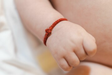 Closeup of a small hand of a newborn baby with a red bracelet encircling the wrist - Powered by Adobe