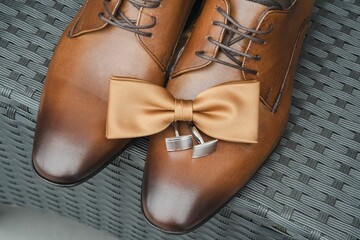 Pair of brown leather shoes with a decorative bow tie accent resting on a woven patterned seat chair