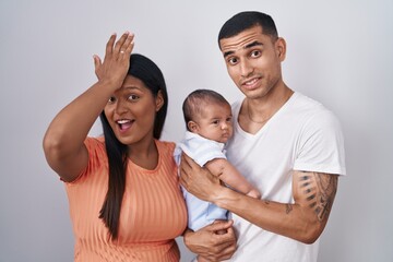 Young hispanic couple with baby standing together over isolated background surprised with hand on...