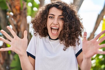 Hispanic woman with curly hair standing outdoors celebrating victory with happy smile and winner...