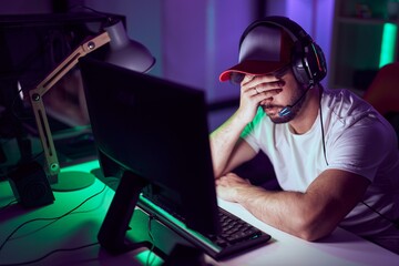 Young hispanic man streamer stressed using computer and headphones at gamin room
