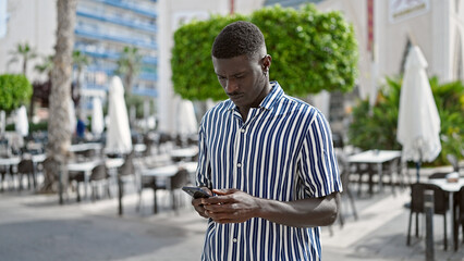 African american man using smartphone with serious expression at coffee shop terrace