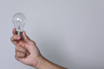Hand holds light bulb on white background. Demonstrates energy savings, copy space