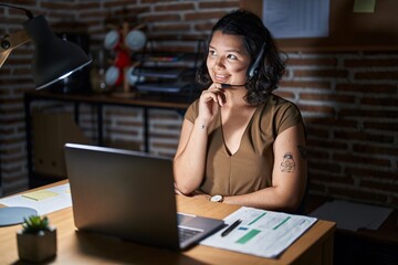 Young hispanic woman working at the office at night with hand on chin thinking about question, pensive expression. smiling and thoughtful face. doubt concept.