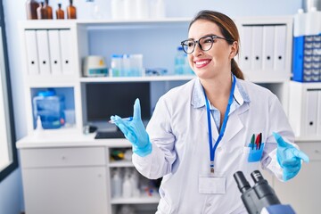 Young beautiful hispanic woman scientist using microscope speaking at laboratory