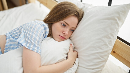 Young blonde woman lying on bed with serious face at bedroom