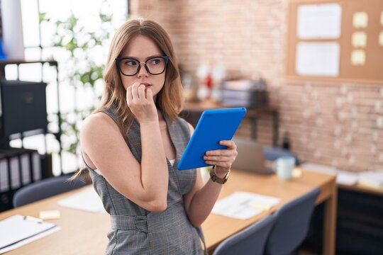 Caucasian woman working at the office wearing glasses looking stressed and nervous with hands on mouth biting nails. anxiety problem.