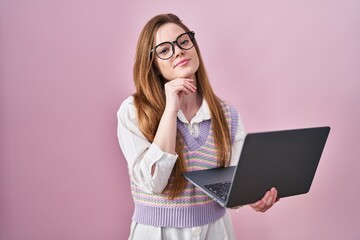 Young caucasian woman working using computer laptop with hand on chin thinking about question, pensive expression. smiling and thoughtful face. doubt concept.