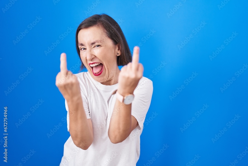 Wall mural middle age hispanic woman standing over blue background showing middle finger doing fuck you bad exp