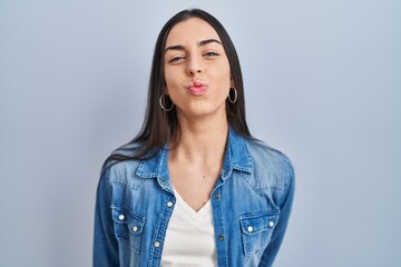 Hispanic woman standing over blue background looking at the camera blowing a kiss on air being...