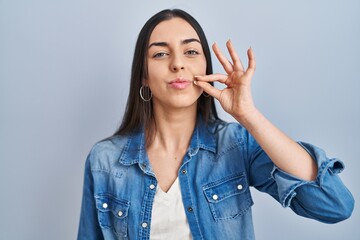 Hispanic woman standing over blue background mouth and lips shut as zip with fingers. secret and silent, taboo talking - obrazy, fototapety, plakaty