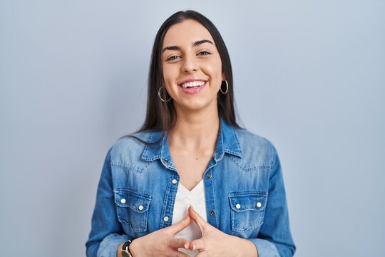 Hispanic woman standing over blue background hands together and fingers crossed smiling relaxed and cheerful. success and optimistic