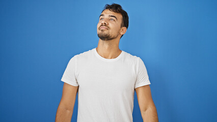Young hispanic man standing with serious expression over isolated blue background
