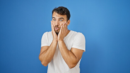 Young hispanic man standing with surprise expression over isolated blue background