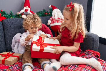 Obraz na płótnie Canvas Adorable boy and girl celebrating christmas unpacking gift at home