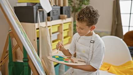 Adorable blond boy artist confidently sitting on chair, drawing at indoor art studio, embodying creativity