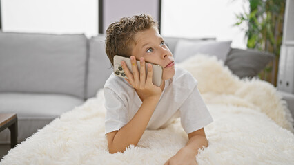 Adorable blond boy, deeply engrossed in a serious phone conversation, lies relaxed on a sofa at...