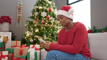 Obraz na płótnie Canvas African american woman celebrating christmas using smartphone at home