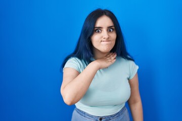 Young modern girl with blue hair standing over blue background cutting throat with hand as knife, threaten aggression with furious violence