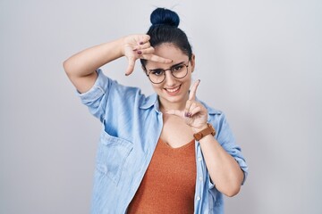 Young modern girl with blue hair standing over white background smiling making frame with hands and fingers with happy face. creativity and photography concept.
