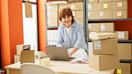 Fototapeta na wymiar Middle age woman ecommerce business worker using laptop smiling at office