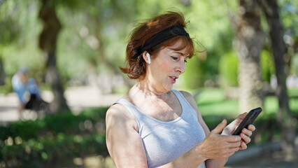 Middle age woman using smartphone and earphones smiling at park