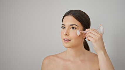 Young beautiful hispanic woman massaging face using skin gym over isolated white background