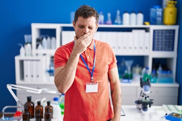 Young hispanic man working at scientist laboratory feeling unwell and coughing as symptom for cold...