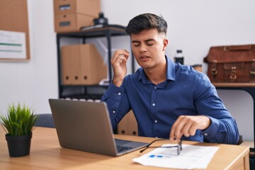 Young hispanic man business worker stressed using laptop at office