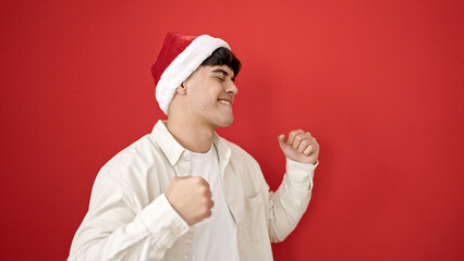 Fototapeta na wymiar Young hispanic man smiling confident wearing christmas hat dancing over isolated red background