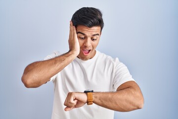 Hispanic man standing over blue background looking at the watch time worried, afraid of getting late