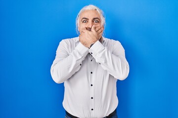 Middle age man with grey hair standing over blue background shocked covering mouth with hands for mistake. secret concept.