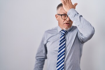 Hispanic business man with grey hair wearing glasses surprised with hand on head for mistake,...