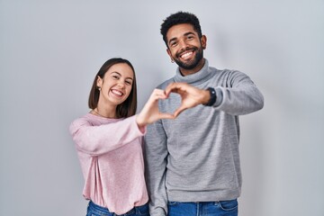 Young hispanic couple standing together smiling in love doing heart symbol shape with hands....