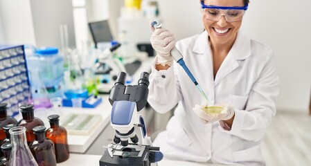 Young beautiful hispanic woman scientist smiling confident pouring liquid on sample at laboratory