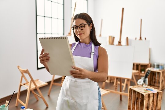 Young beautiful hispanic woman artist smiling confident looking draw on notebook at art studio