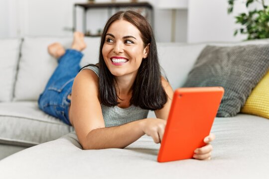 Young beautiful hispanic woman using touchpad lying on sofa at home