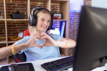 Young caucasian woman playing video games wearing headphones smiling in love doing heart symbol shape with hands. romantic concept.