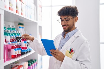 Young arab man pharmacist using touchpad holding medicine bottle at pharmacy
