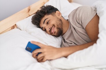 Young arab man using smartphone lying on bed at bedroom